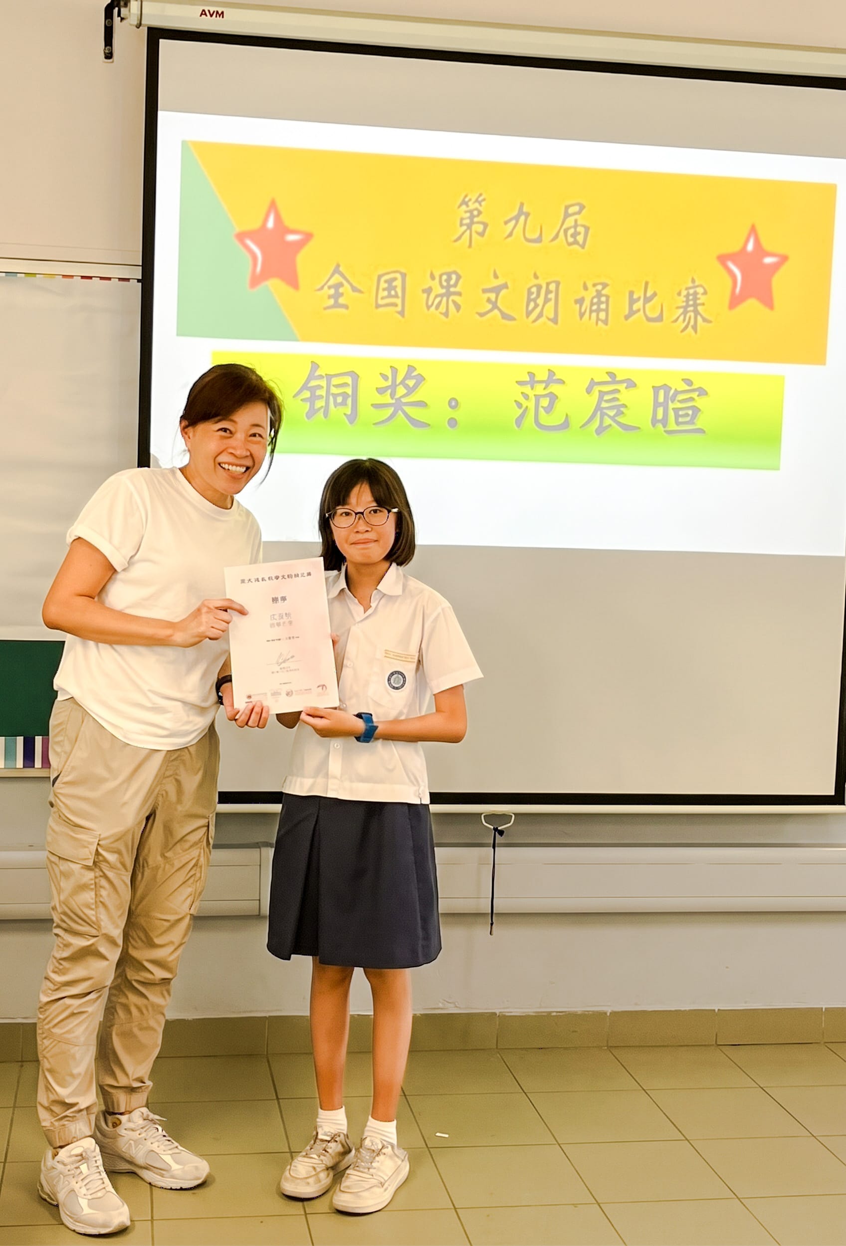 Primary 5 student Alice Fan (Fan Chenxuan) holding her Bronze Award certificate alongside HOD Chinese Language.